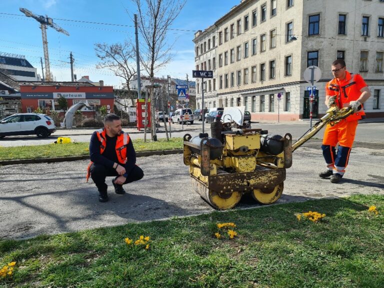 Werkemeister Aleksandar Begovic kontrolliert die ordnungsgemäße Instandsetzung von Straßenschäden und beobachtet, wie ein Arbeiter den Untergrund mit einer handgeführten Walze verdichtet.